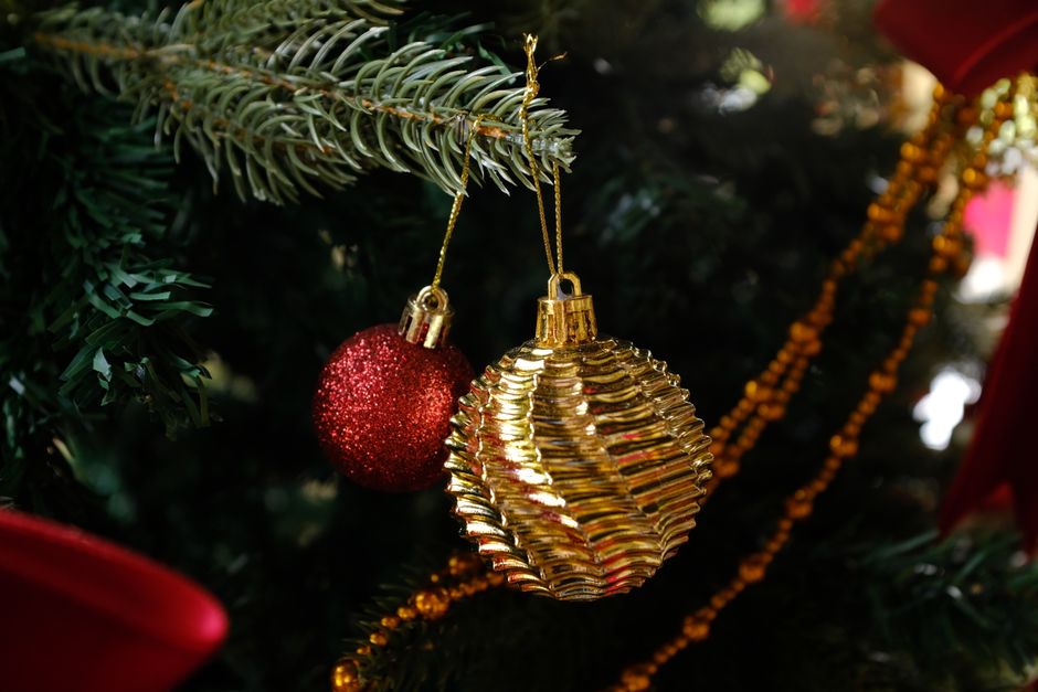 Close-up of gold and red Christmas ornaments hanging on an evergreen branch.