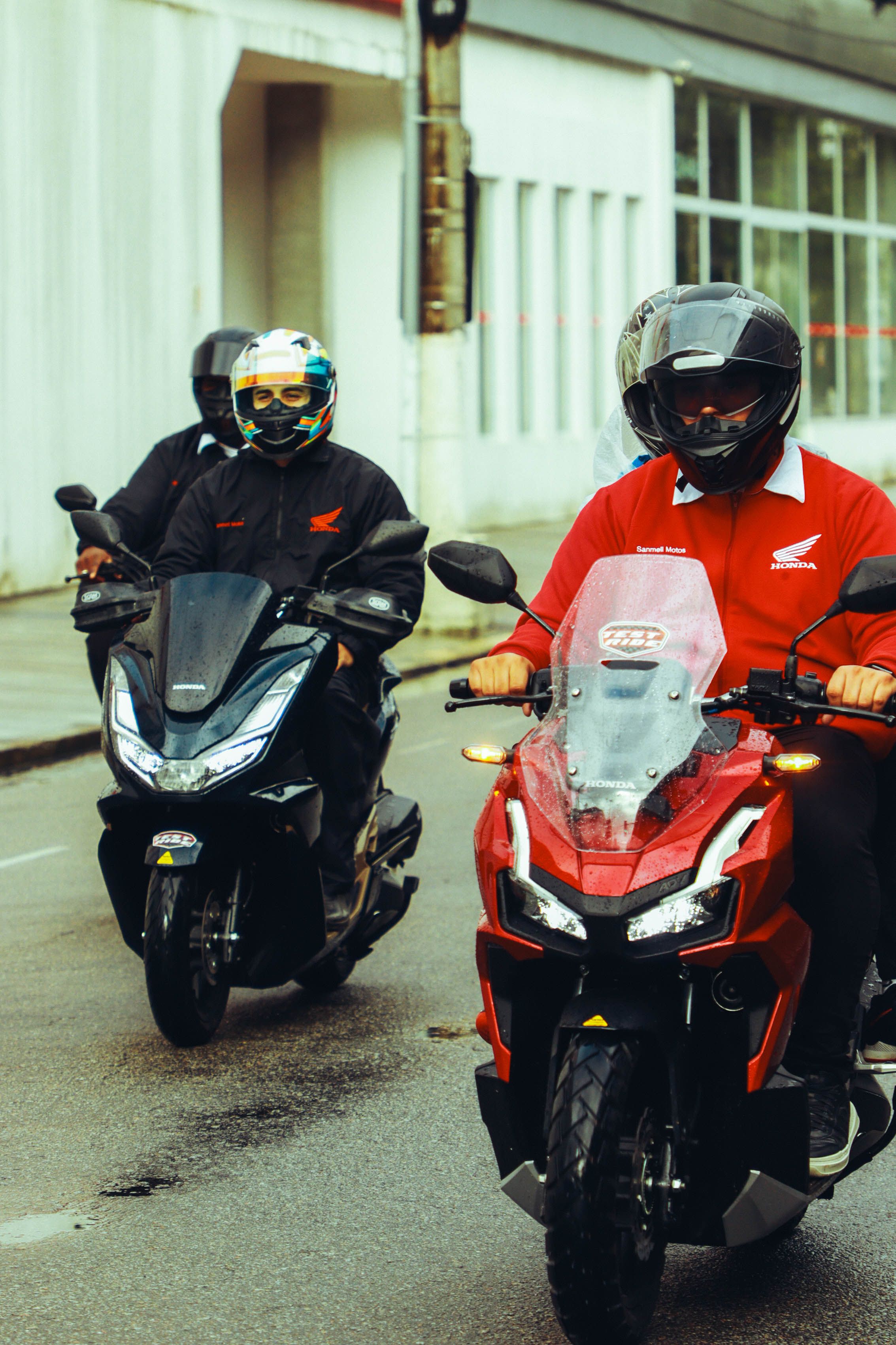 Motorcyclists wearing helmets ride Honda motorcycles on wet streets in Santos, Brazil.