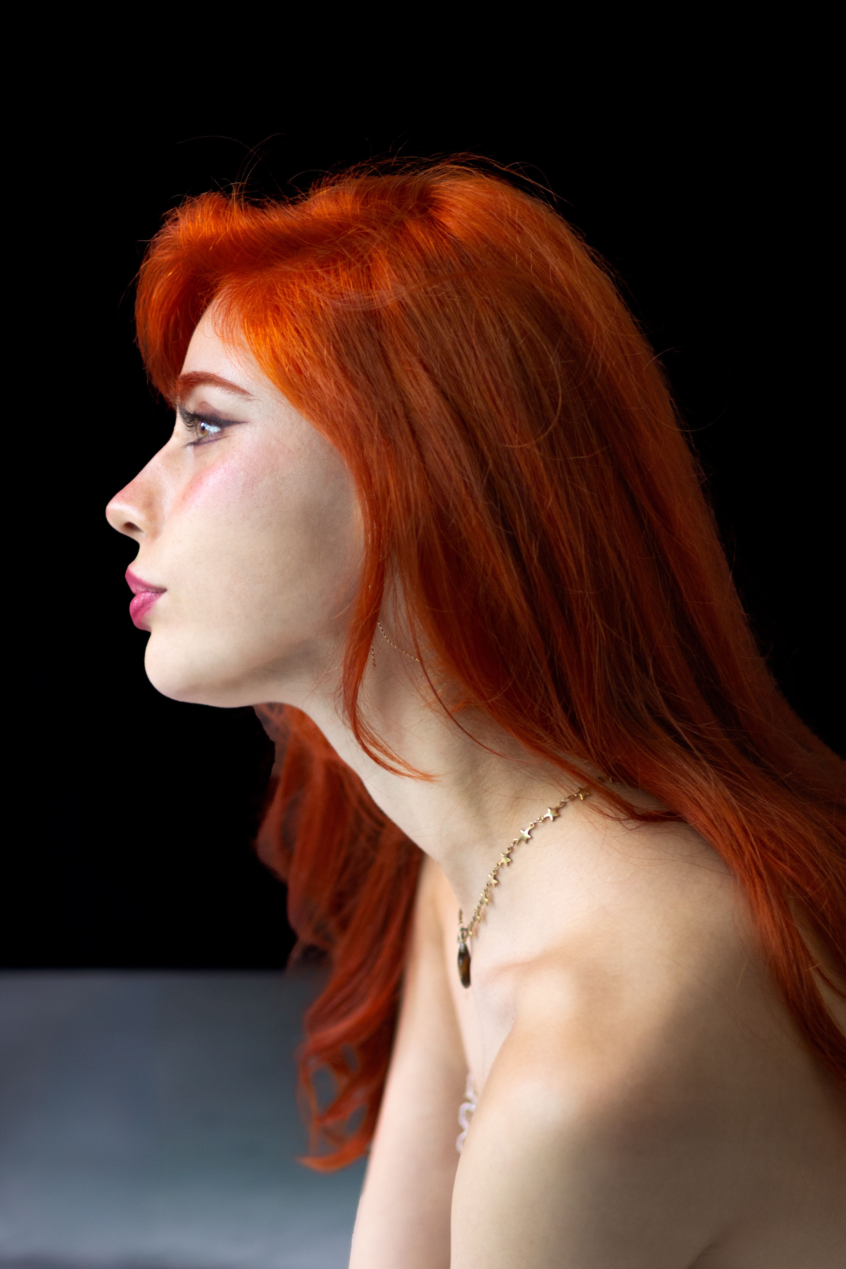 Side profile of a woman with striking red hair against black background.