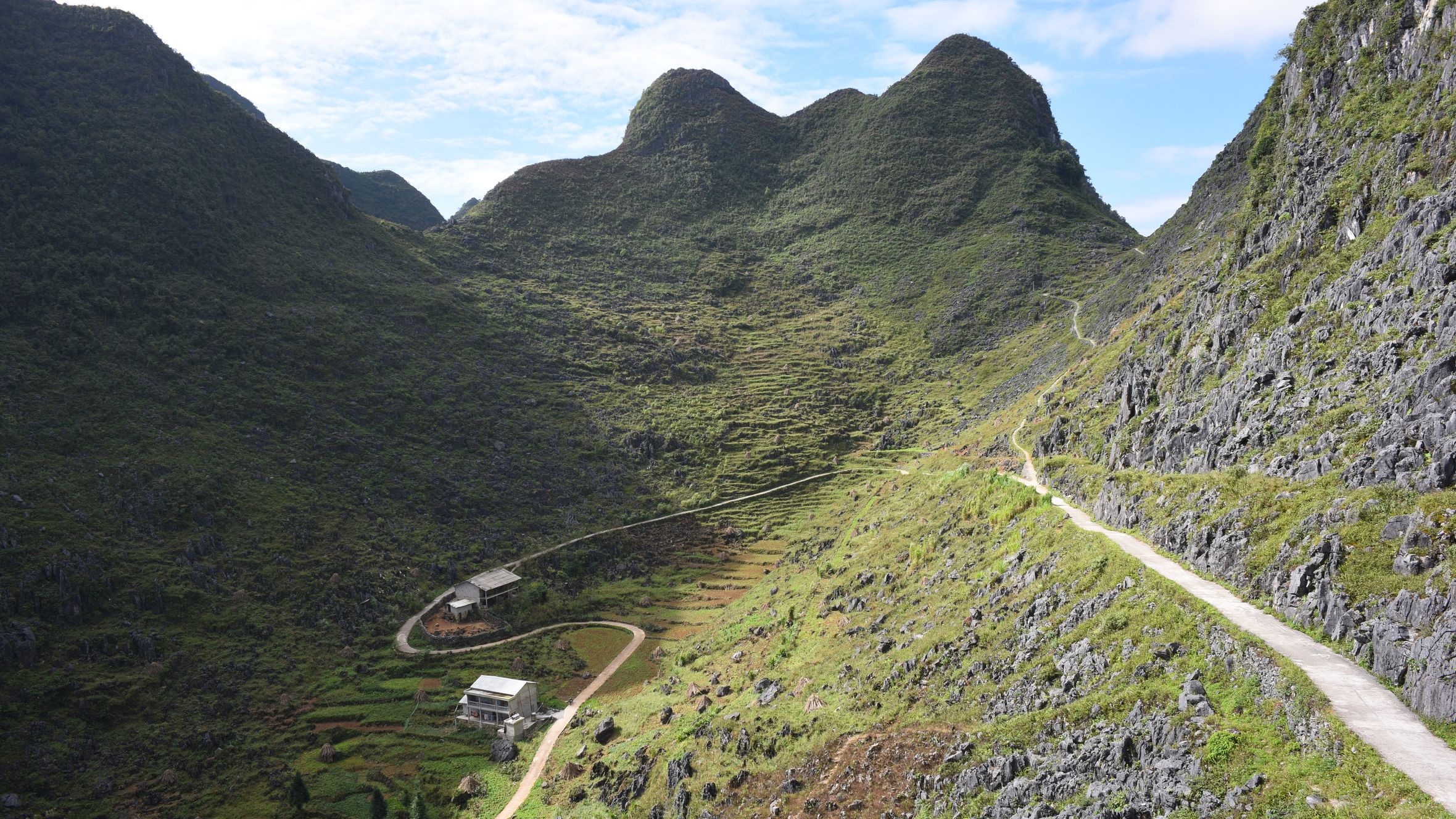 Beautiful mountain valley with greenery and a winding path under a clear blue sky.