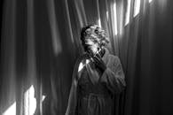 一名穿着浴衣的女子倚在窗帘边，阳光洒落，投下摇曳的影子