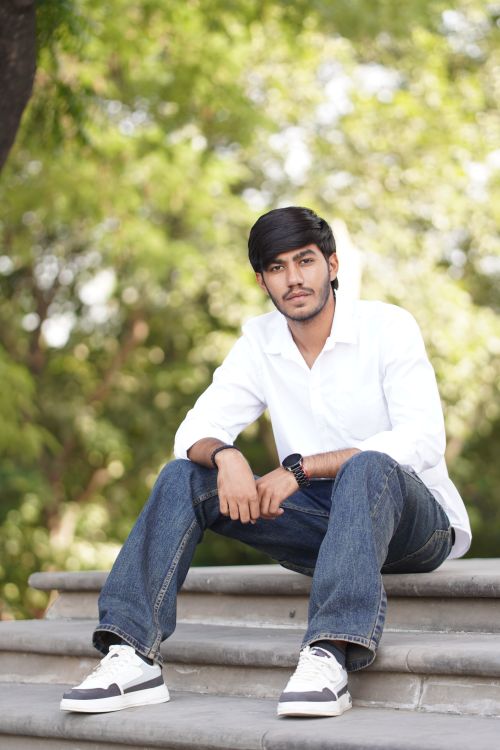 Free Young man sitting casually on outdoor steps in a white shirt and jeans. Stock Photo