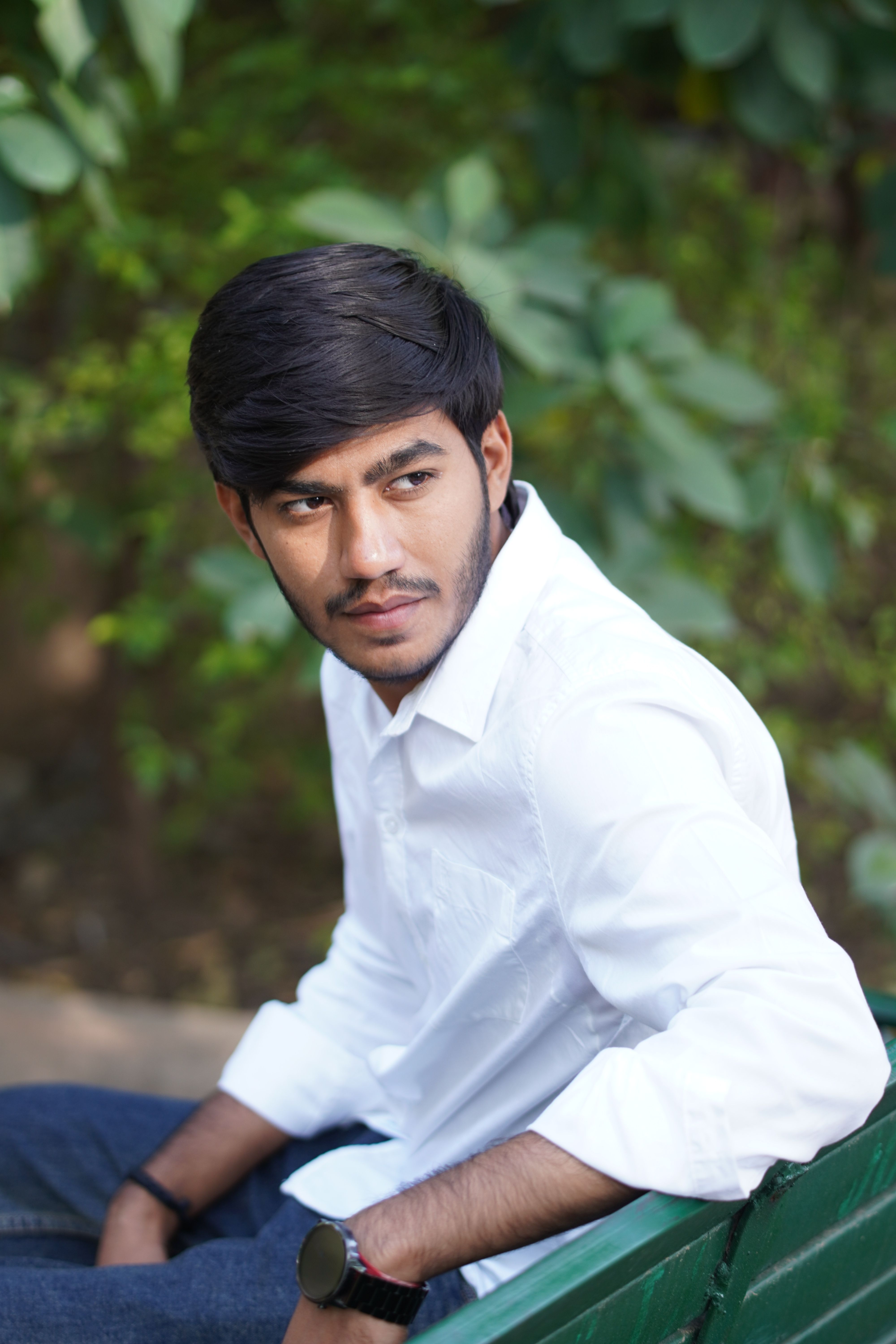 Pensive young man in a white shirt sitting on a park bench, outdoors.