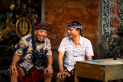 Free Two Indonesian men smiling and laughing while sitting outdoors in traditional clothing. Stock Photo