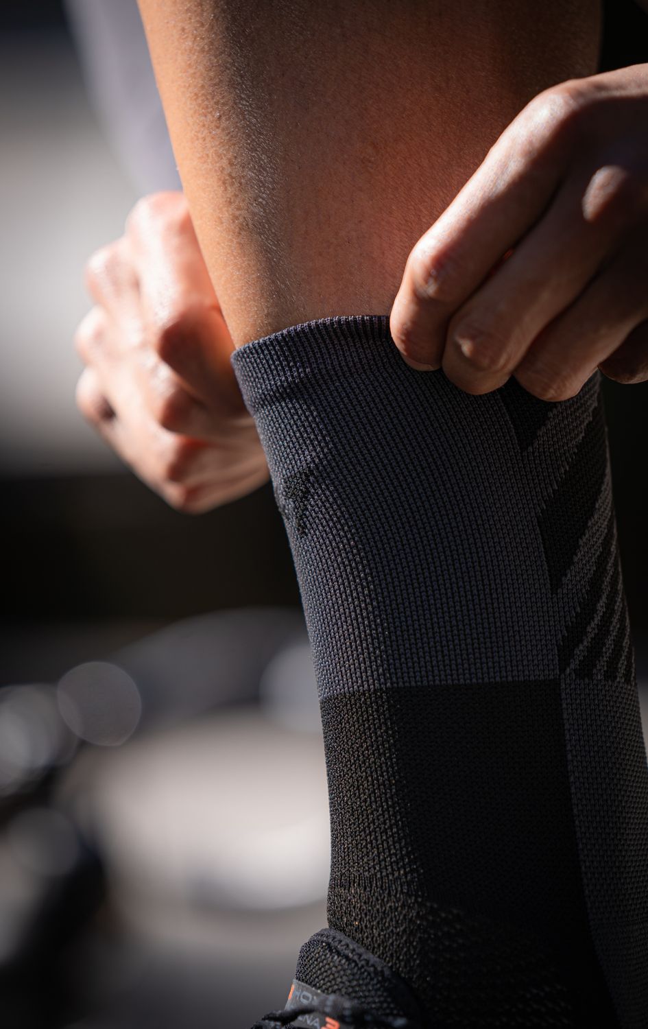 Close-up of a person adjusting a gray athletic compression sock on their leg