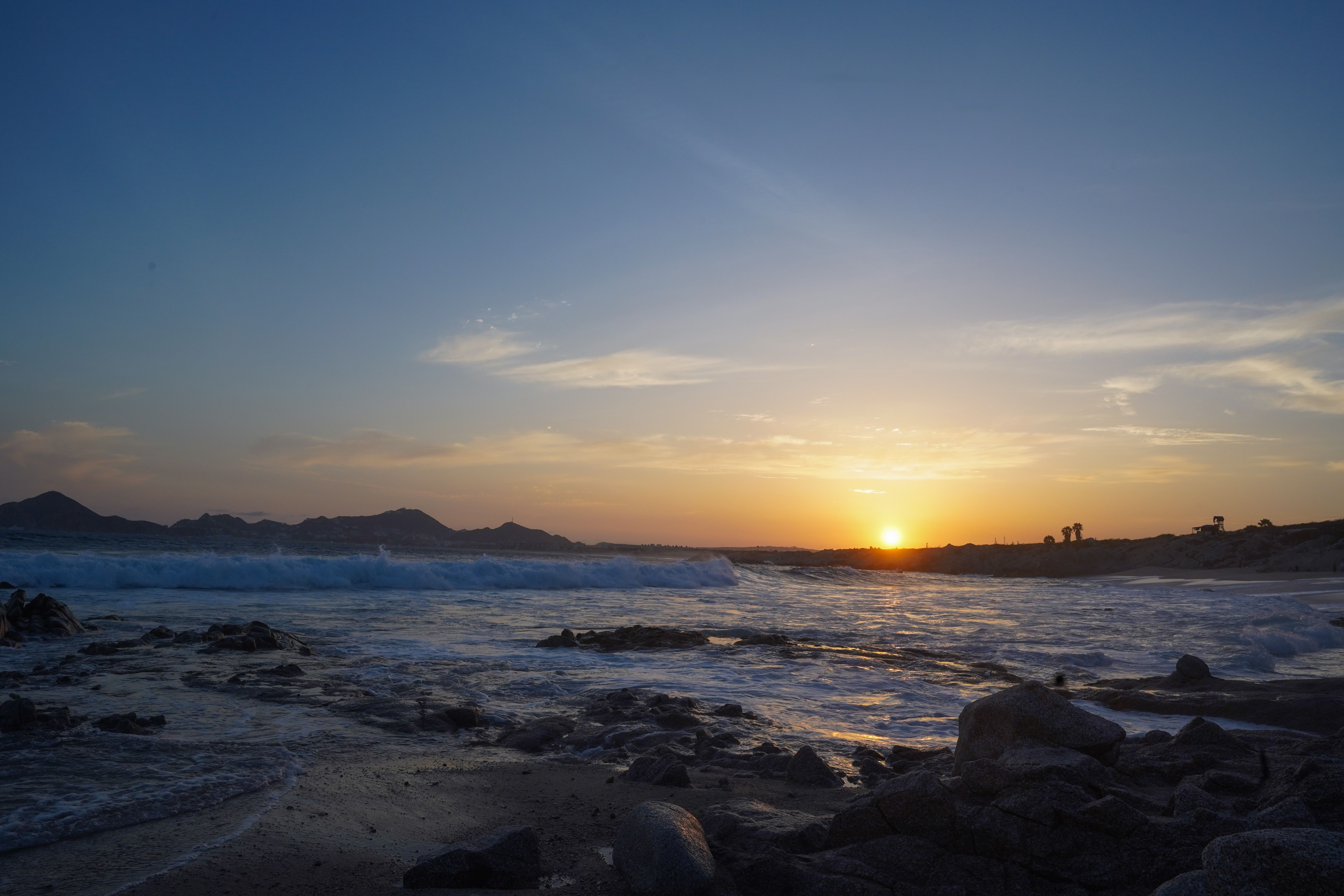 Serene Beach Sunset Over Rocky Shoreline · Free Stock Photo