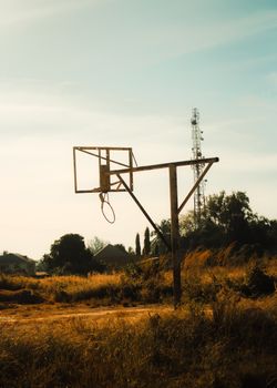 An old wooden basketball hoop on a rural field during sunset, exuding a nostalgic feel.