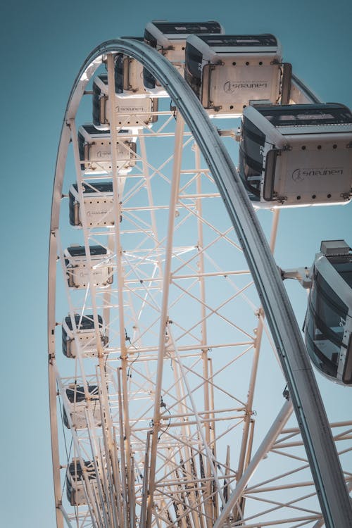 From below of contemporary Ferris wheel with white cabins in city amusement park in bright sunny day