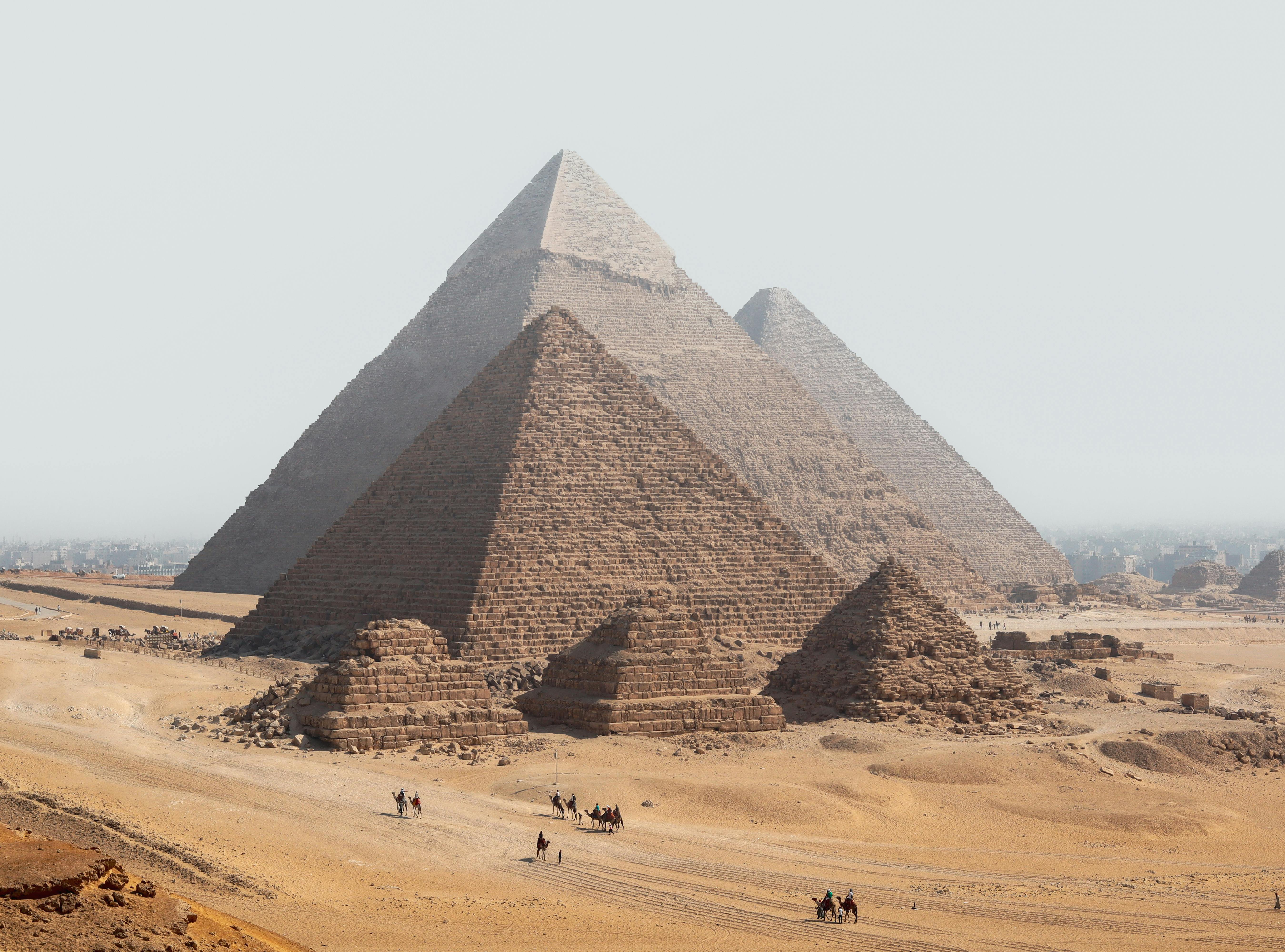 Gratis Vista panoramica delle piramidi di Giza con cammelli nel deserto sotto un cielo limpido. Foto a disposizione