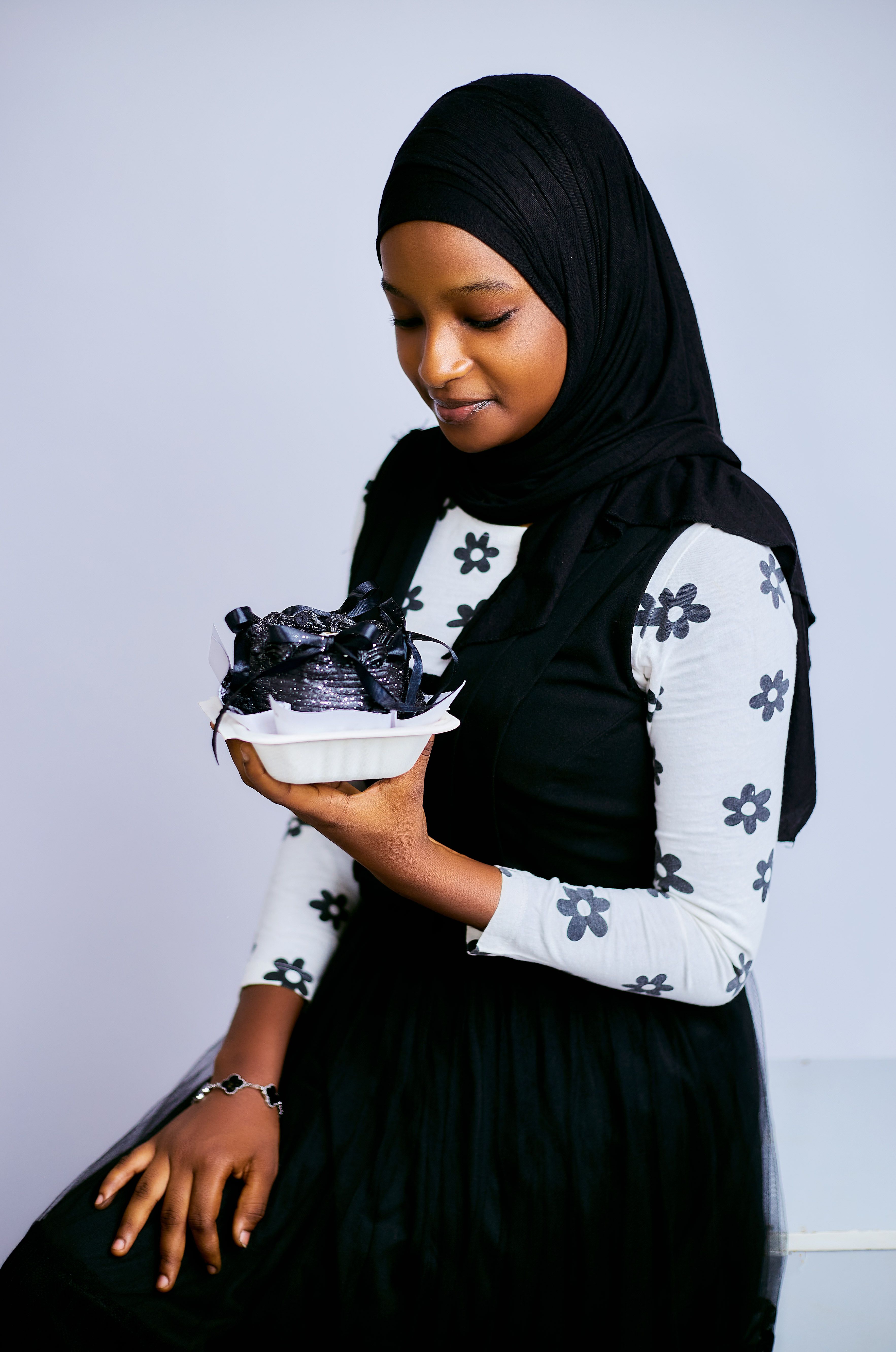 A young woman in a black hijab admires a beautifully wrapped gift box indoors.