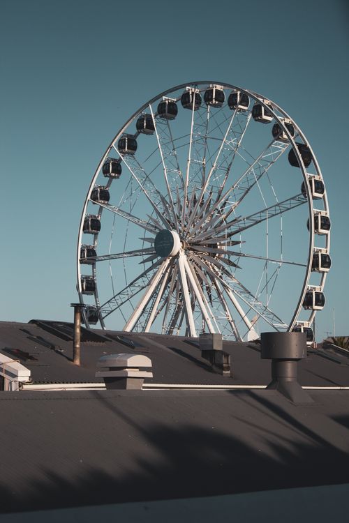 Free Ferris wheel towering over rooftops against a clear sky on a sunny day. Stock Photo