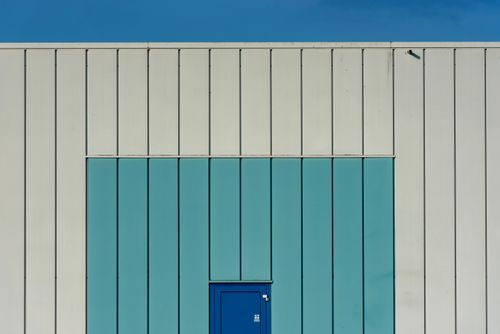 Free Abstract view of a minimalist building facade featuring a blue door and vertical lines. Stock Photo