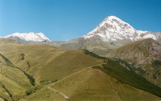 Scenic landscape photo of the snow-capped Mount Kazbek against a clear blue sky.
