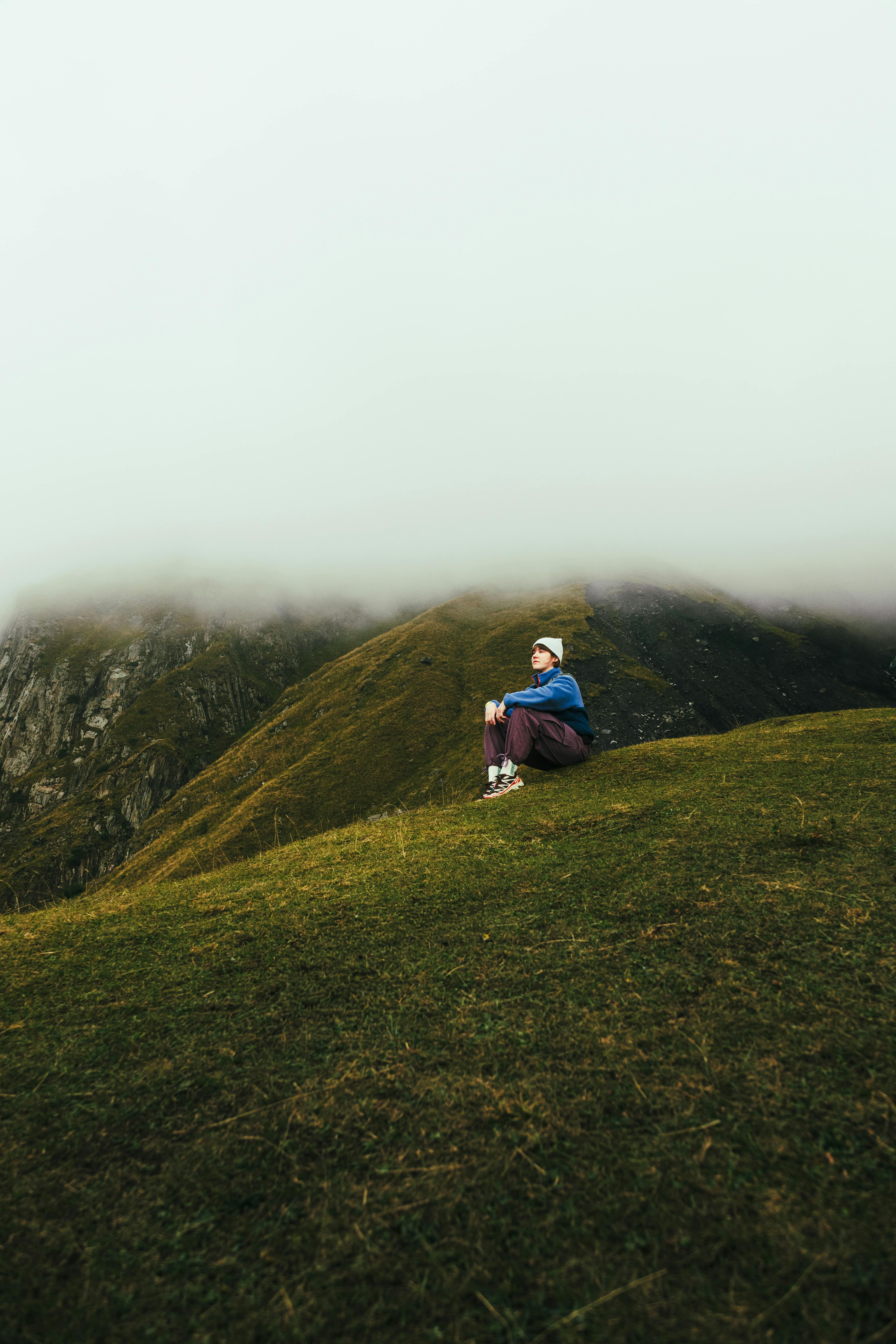 Person sitting on a misty mountain slope, embracing solitude and nature's tranquility.