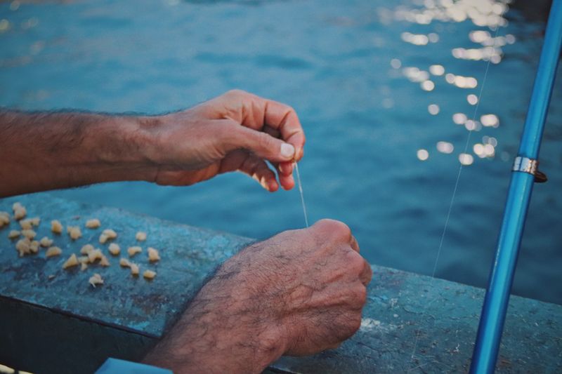 Hands preparing fishing line at the waterfront, close-up of line handling