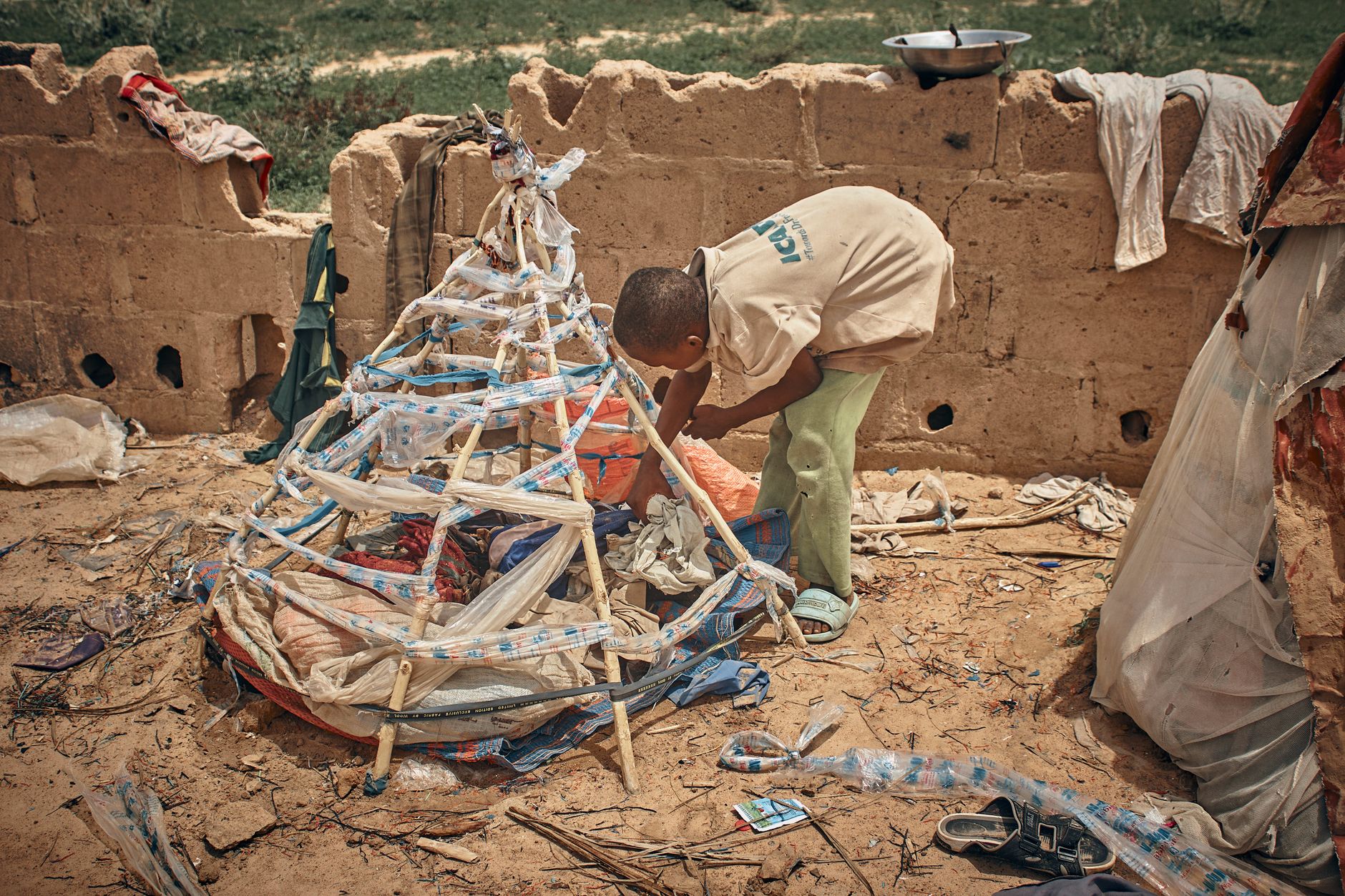 A young African child constructing a makeshift shelter with recycled materials in a rural setting.