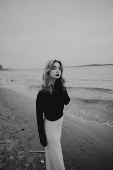 Black and white portrait of a woman on a beach, evoking a moody and dramatic atmosphere.