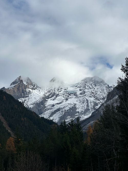 Free Snow-capped peaks of a mountain range under a cloudy sky, with lush forest at the base. Stock Photo