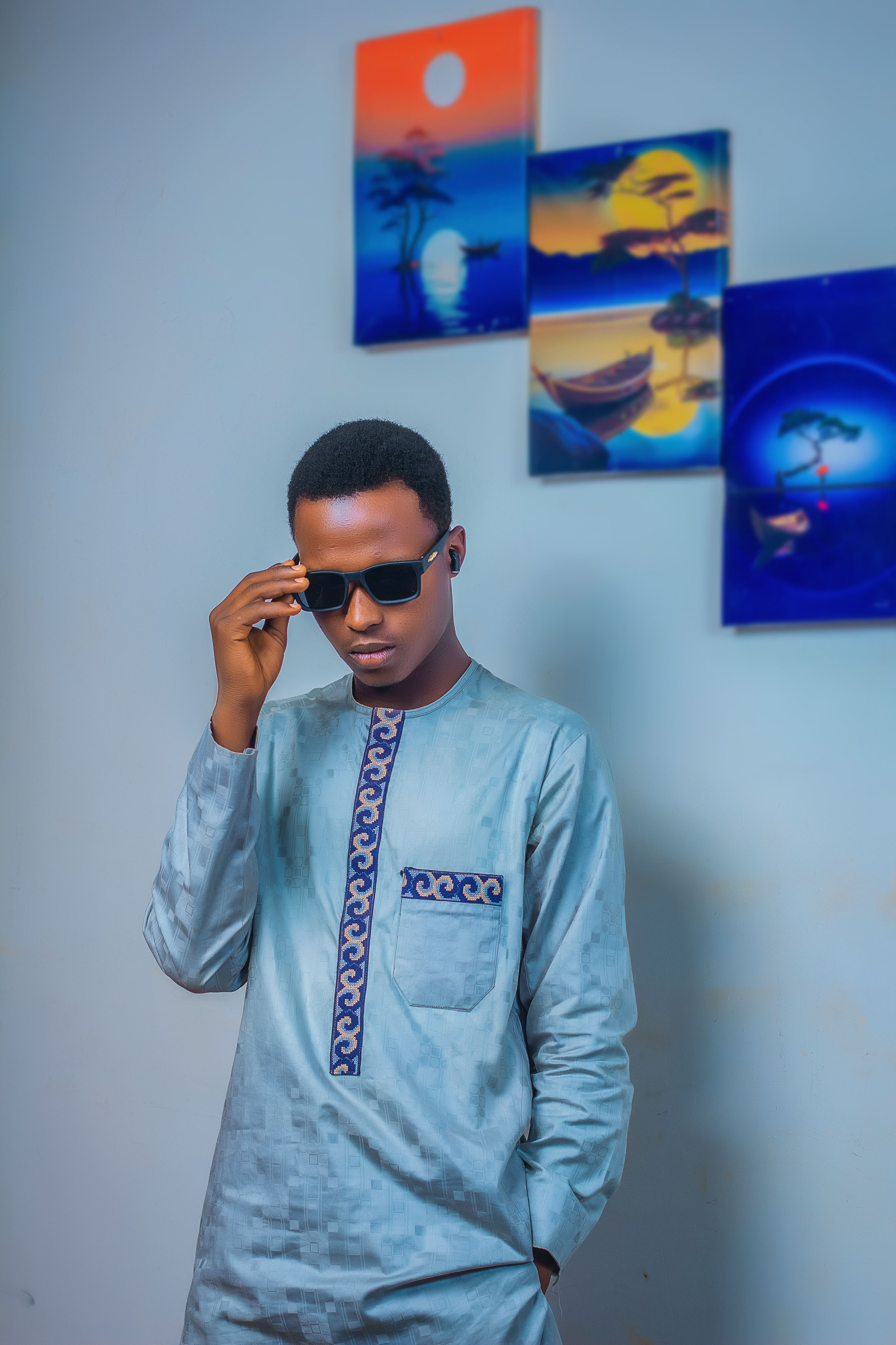 Young man wearing traditional clothing and sunglasses with abstract artwork in the background.