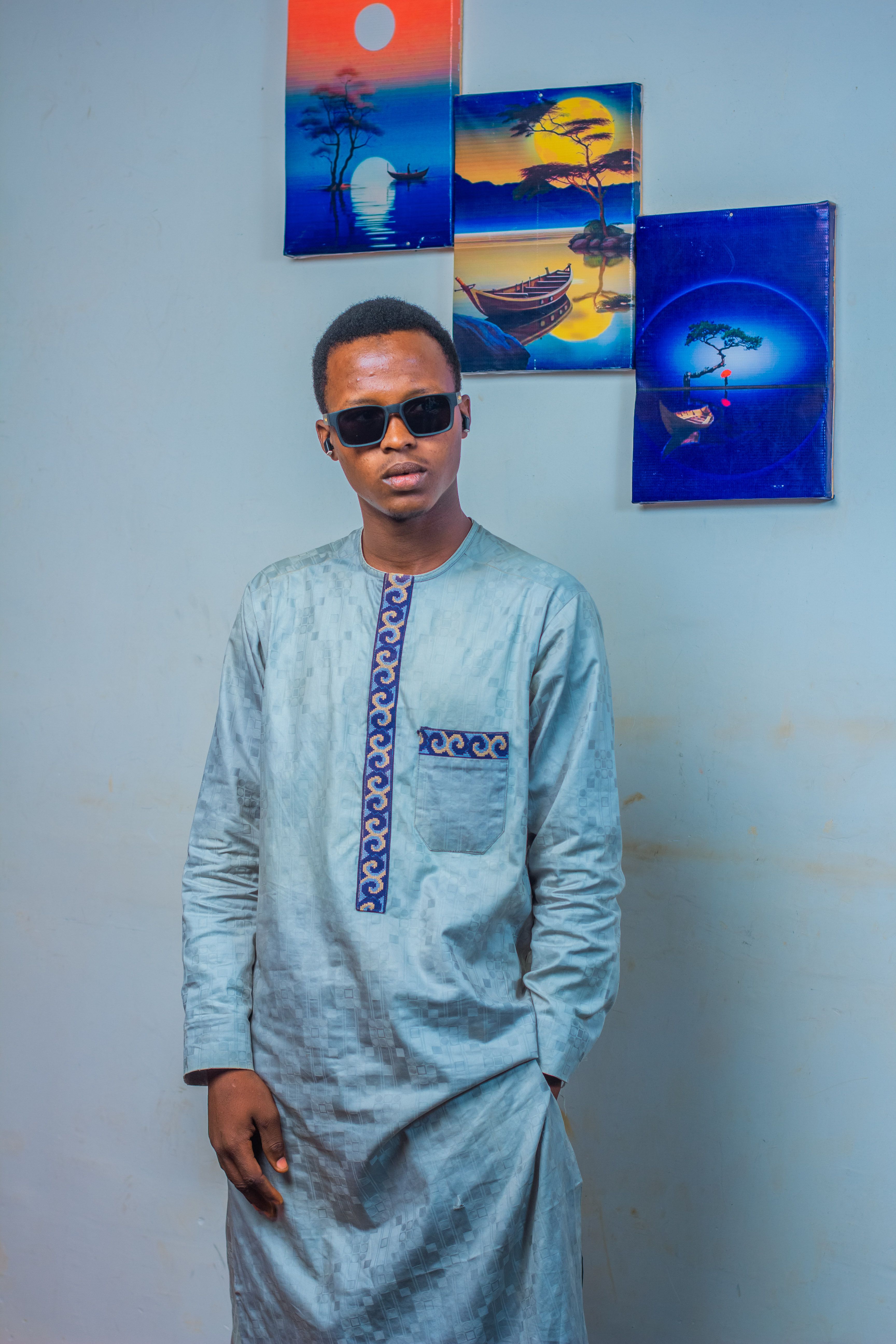 A young man wearing traditional clothing poses stylishly in a room with artistic wall decor.