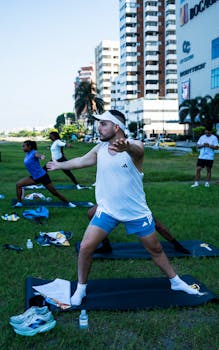 Group practicing yoga outdoors in city park with modern buildings. Fitness and wellness lifestyle.