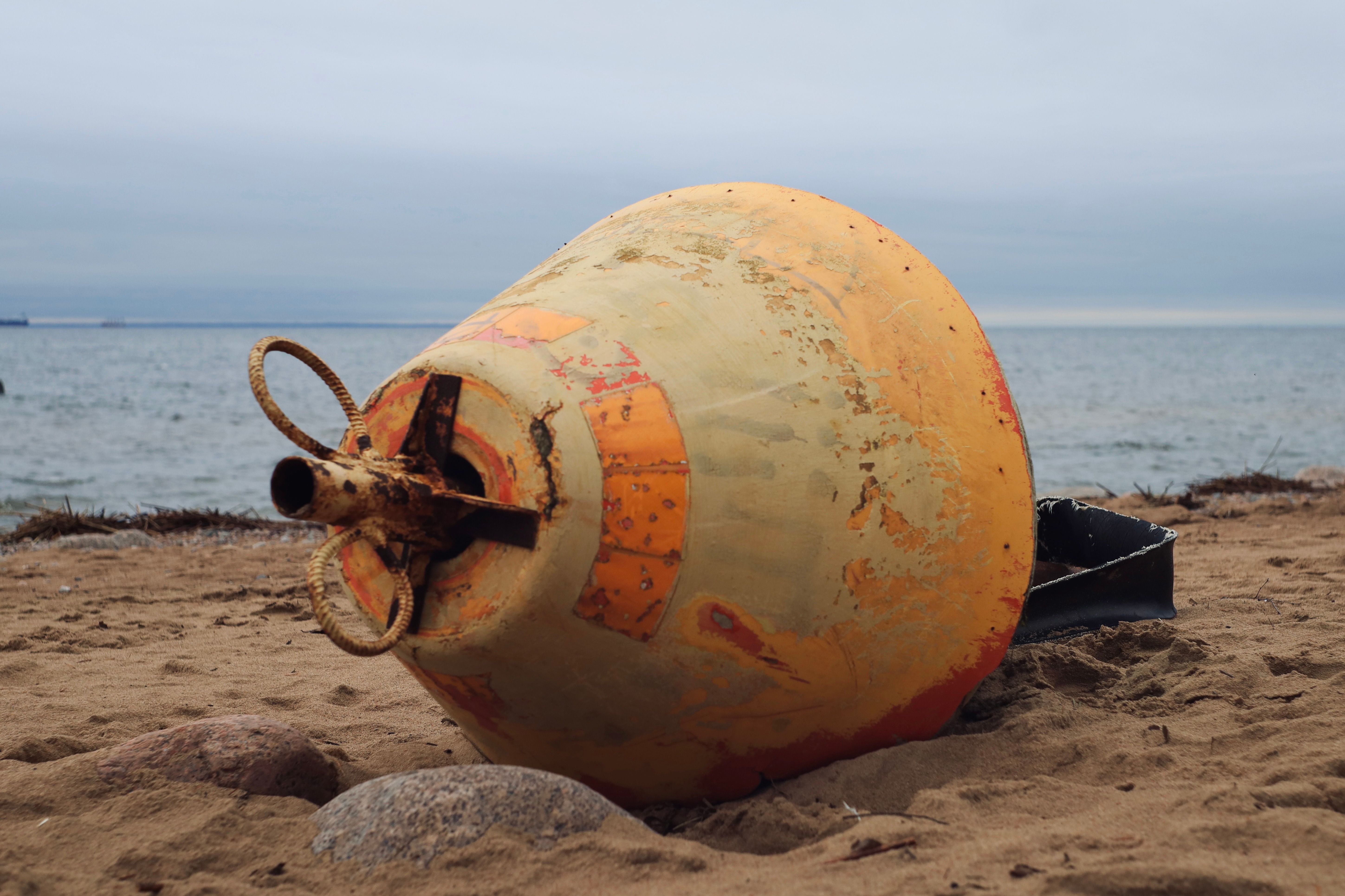 Weathered yellow buoy on a sandy beach near the ocean, creating a coastal ambiance.