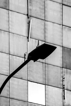 Black and white image of a streetlight in front of a modern, geometric building facade.