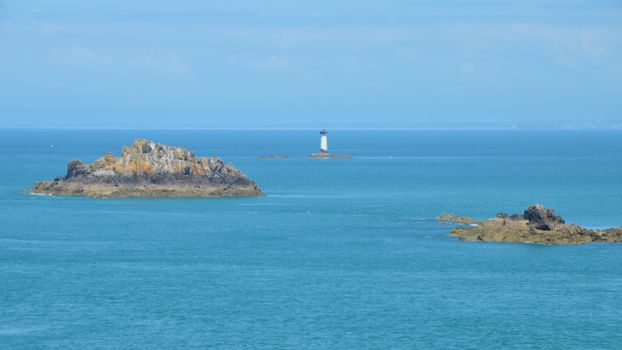 Tranquil ocean view featuring rocky islets and a lighthouse off Cancale's coast in Brittany, France.