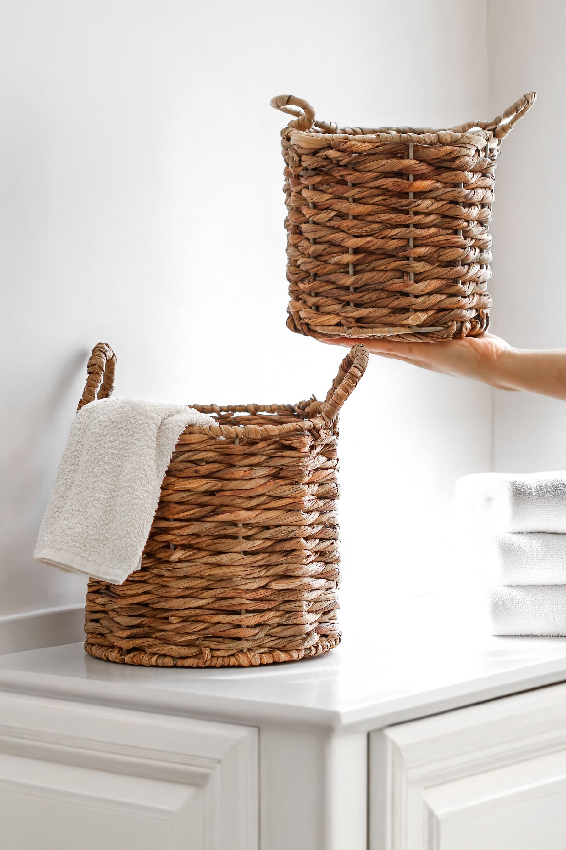 A bright bathroom organized with woven storage baskets, folded towels and shelf containers