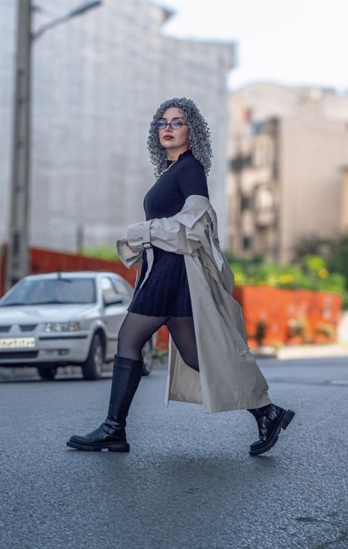 Free Stylish woman in urban setting, wearing trench coat and boots, exuding confidence. Stock Photo
