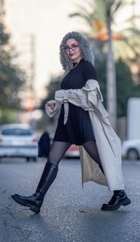 Fashionable woman with curly hair crossing a street in a chic outfit and boots.