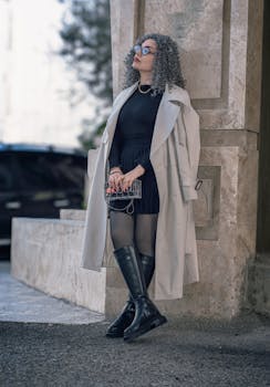 Fashionable woman in a trench coat standing outdoors with urban backdrop.