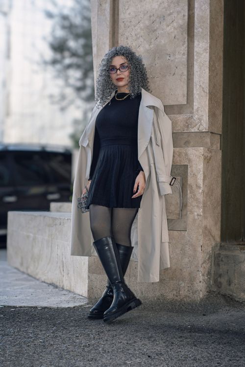 Free Fashionable woman wearing a black dress and trench coat posing by a stone wall outdoors. Stock Photo