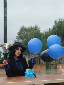 Stylish woman in formal wear celebrates with blue balloons and cake outdoors.