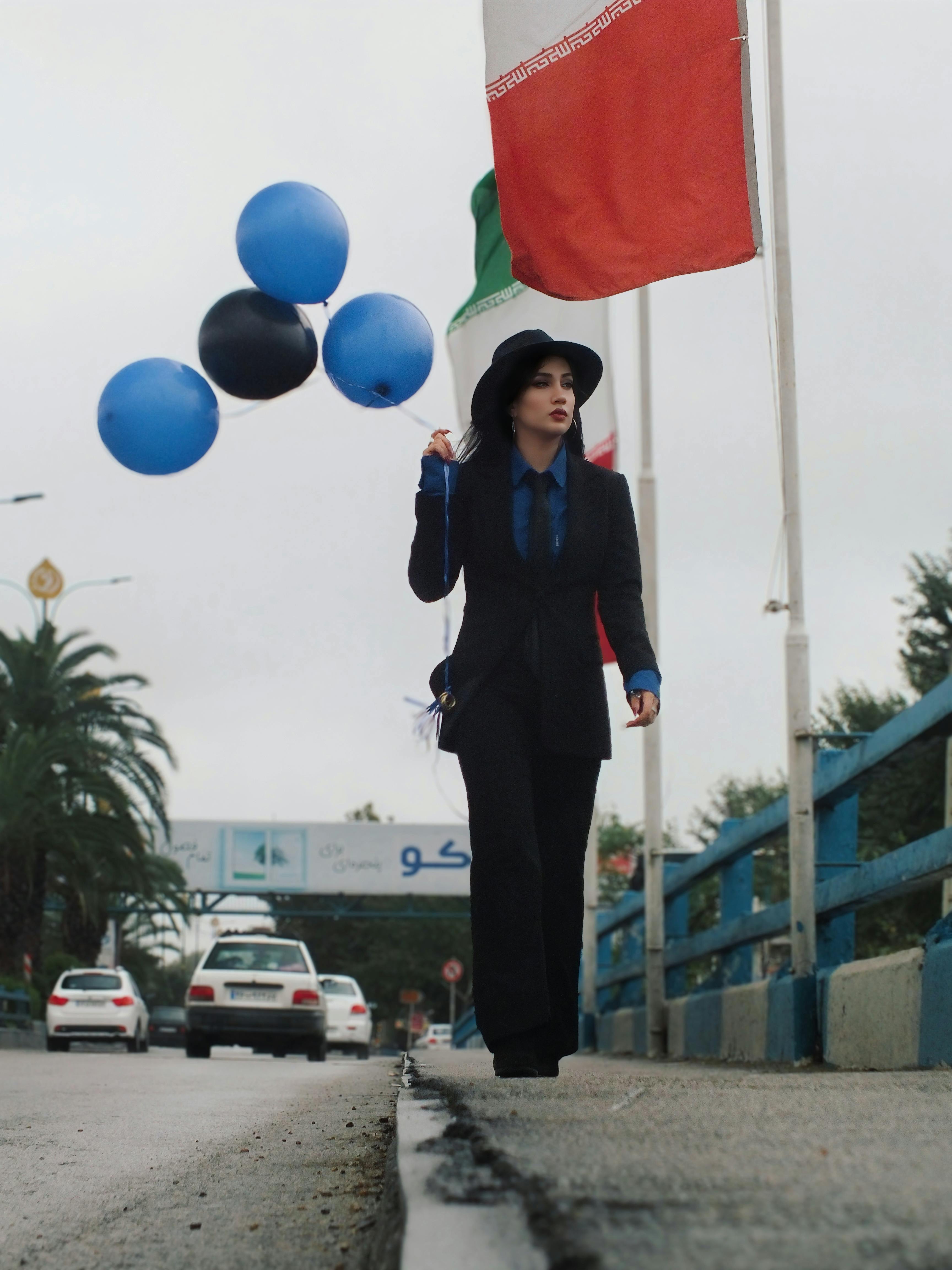 Elegant woman in black suit with balloons walking down a city street lined with flags.