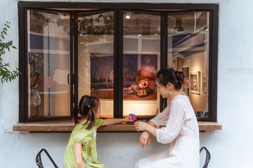 Free A mother and daughter relax at a cafe window seat with art in the background, creating a serene and bonding moment. Stock Photo
