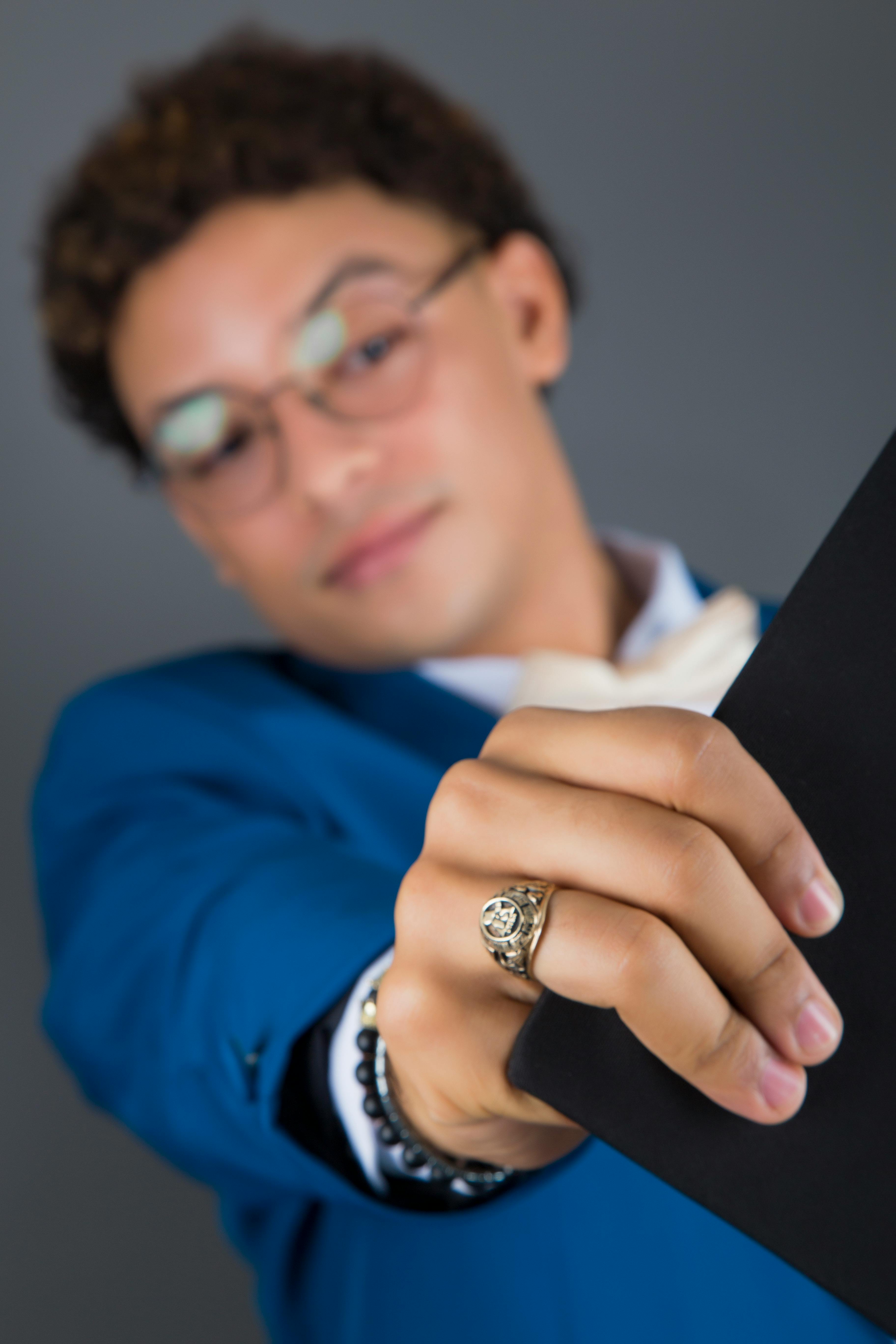 grátis Jovem recém-formado de terno azul exibe orgulhosamente seu diploma contra um fundo cinza neutro. Foto profissional