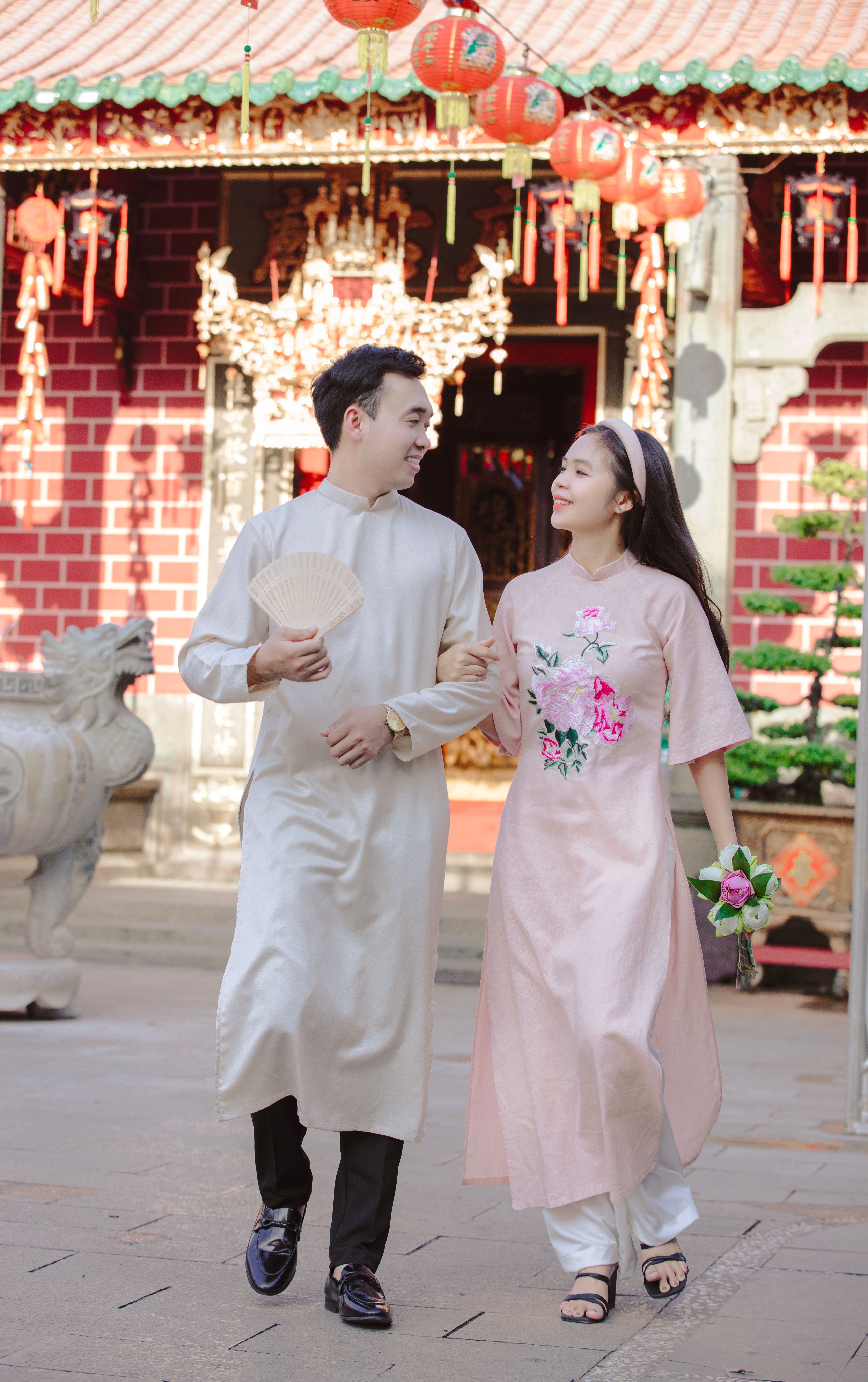 A couple in traditional Vietnamese ao dai walking together in a festive setting with lanterns.