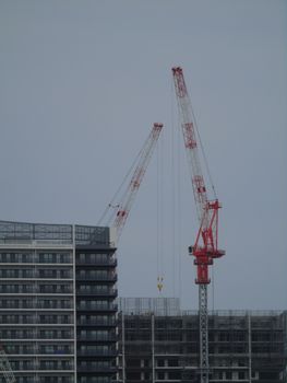 Two tower cranes at a construction site with modern buildings under a cloudy sky.
