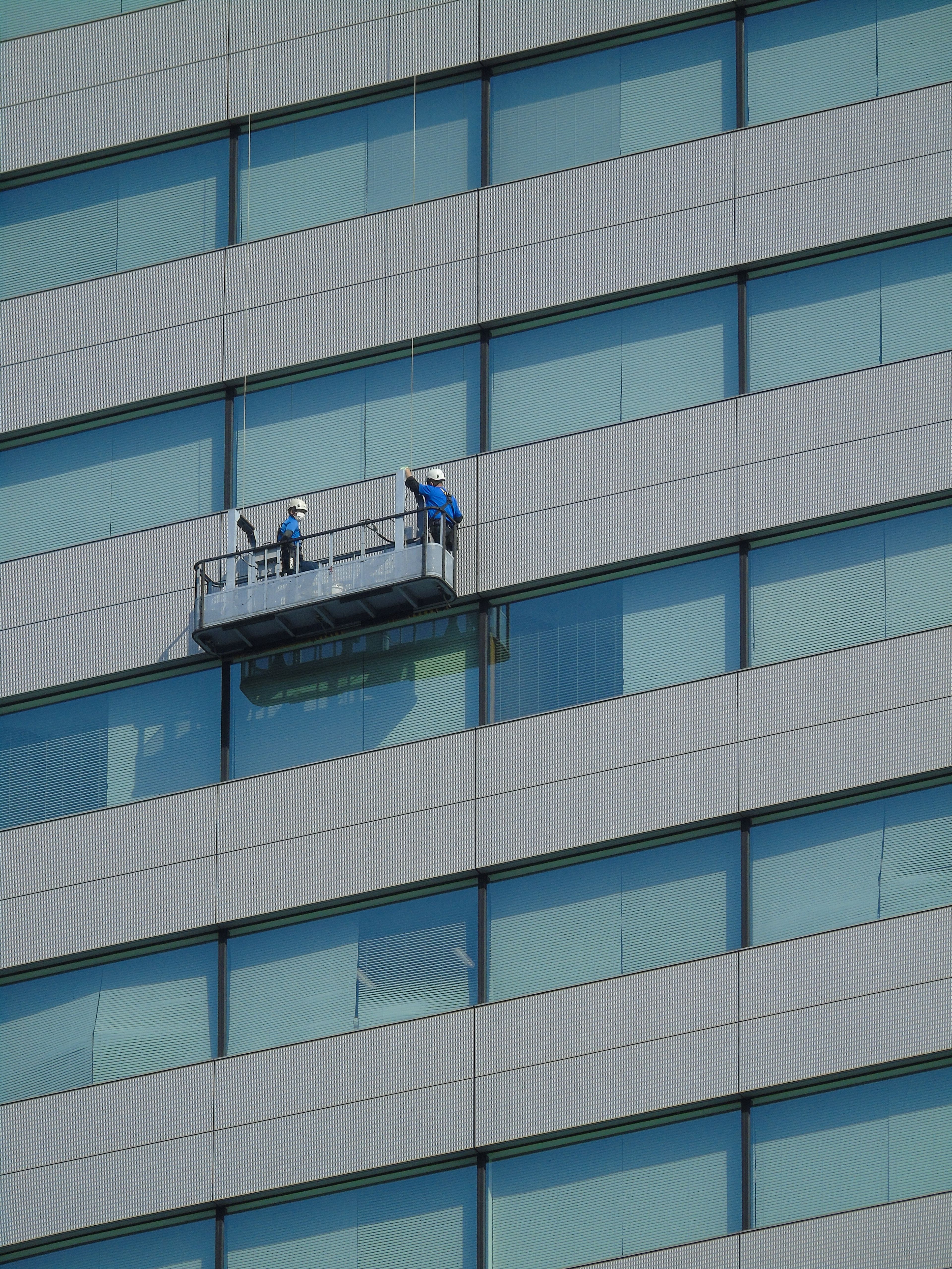 Façade vitrée d'un immeuble contemporain avec deux laveurs de vitres suspendus à mi-hauteur
