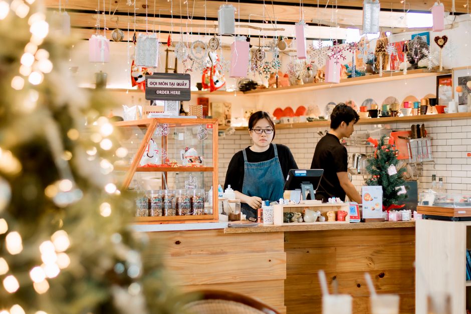 Cozy cafe with Christmas decor, barista at counter, warm atmosphere.