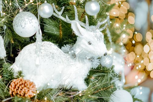 Free Festive white reindeer ornament on a decorated Christmas tree with glowing lights. Stock Photo