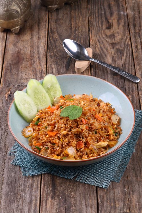 Free Tasty Nasi Goreng with fresh cucumber slices on rustic table setting. Stock Photo