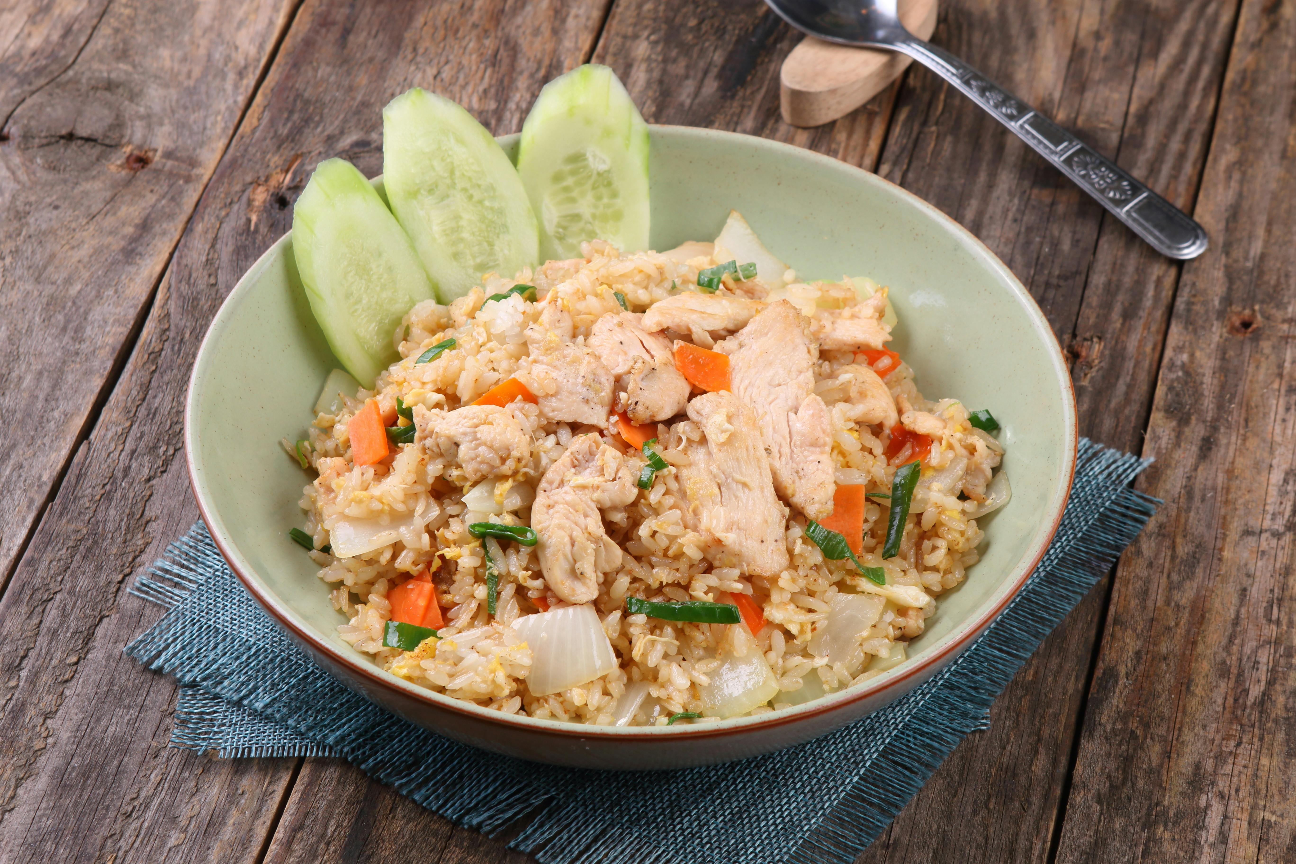 Mouthwatering chicken fried rice with fresh vegetables on rustic wooden table.