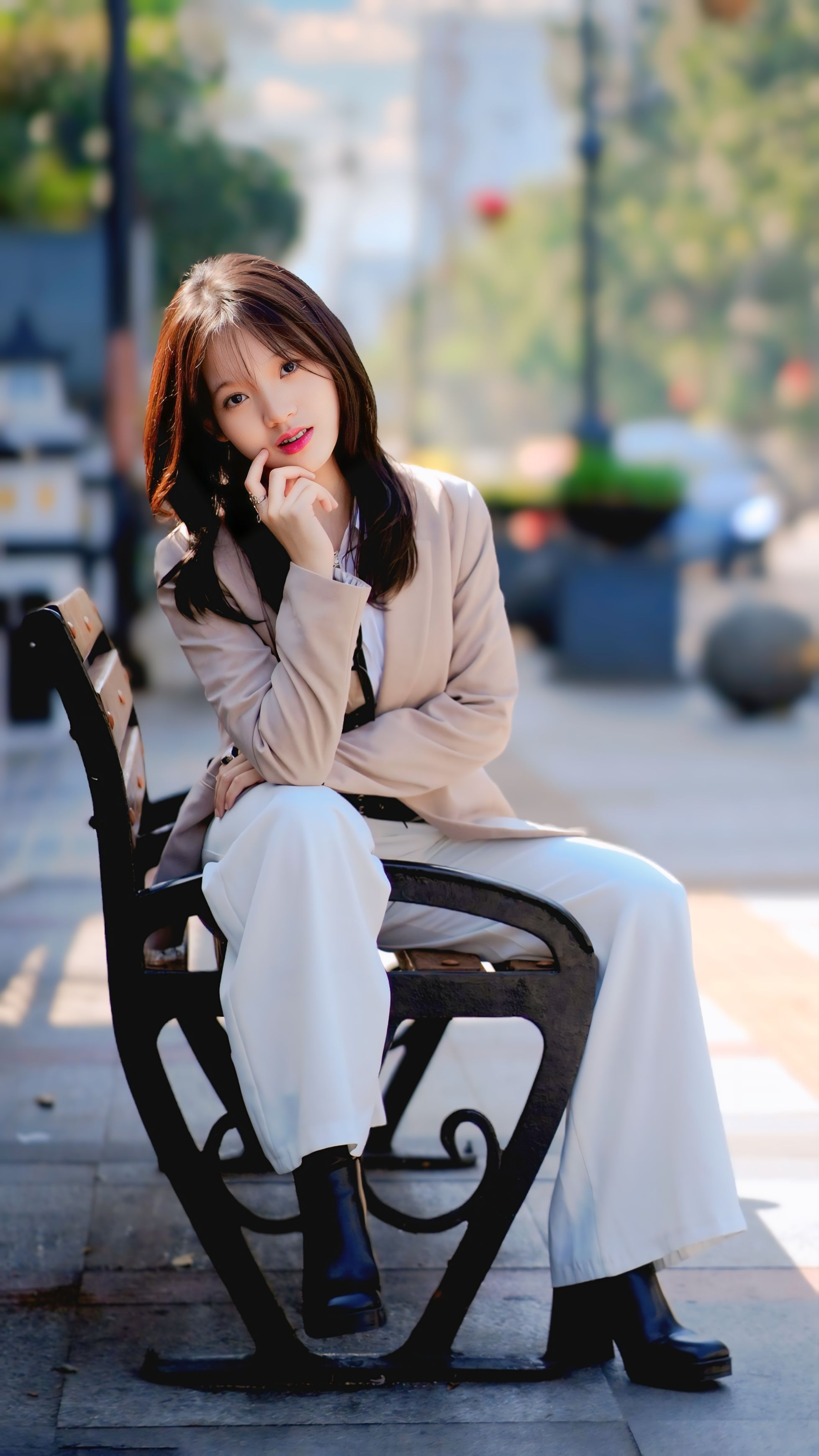 Woman in fashionable attire sitting on a bench in a sunny urban area.