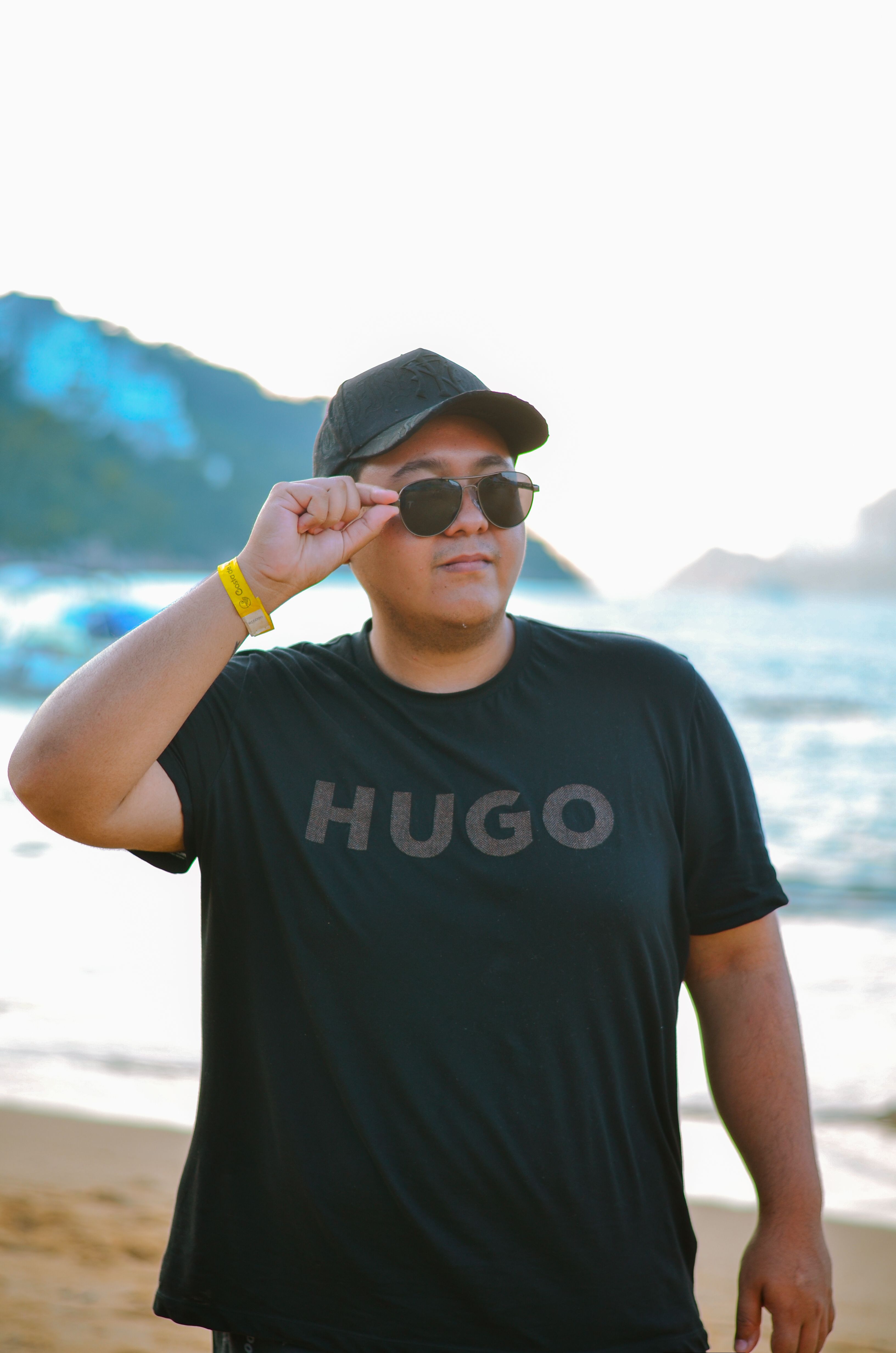 Man in black shirt and cap enjoying a sunny day at the beach, wearing sunglasses.