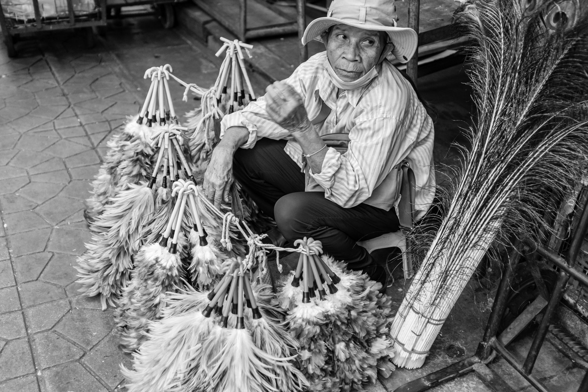 A street vendor sits surrounded by handmade feather dusters, capturing the essence of local market life.