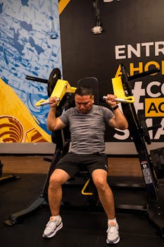 Adult male working out using shoulder press machine at indoor gym. Fitness and strength training focus.
