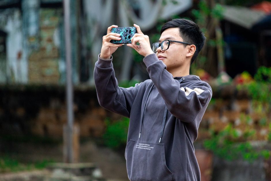 A young man captures a moment with his smartphone outside in Hà Nội, Việt Nam.