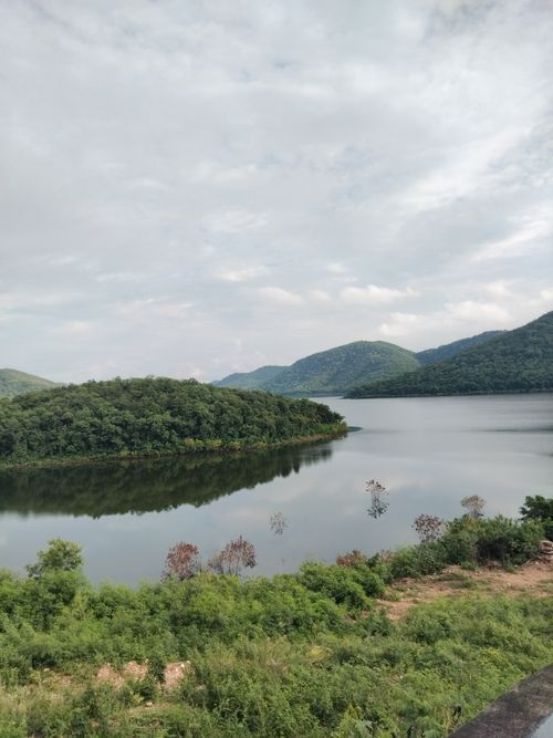 Free Peaceful view of a lake surrounded by green hills under a cloudy sky. Stock Photo